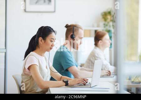 Eine Gruppe von Geschäftsleuten mit Kopfhörern, die am Tisch sitzen und im Büro an einem Laptop arbeiten Stockfoto