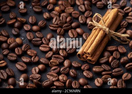 Geröstete braune ganze Kaffeebohnen und gebundene Zimtstangen auf dunklem Hintergrund Stockfoto