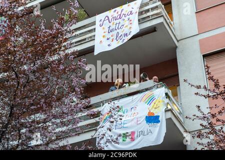 Die Menschen singen, winken und klatschen ihre Hände neben einem Banner mit der Aufschrift 'hastag #andratuttobene, restiamo a casa ' (Komm schon, Jungs #everythingsgonnabeallright, Stockfoto