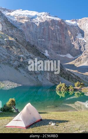 Der Pamir-Bergblick und ruhiger Campingplatz am Kulikalon-See im Fann-Gebirge in Tadschikistan. Aufmunterende bunte Reflexion in reinem Eissee. Stockfoto