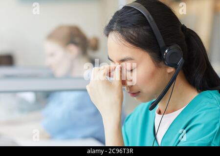 Junge Frau in Kopfhörern müde von der Arbeit hat sie Kopfschmerzen, während sie am Tisch im Büro sitzt Stockfoto