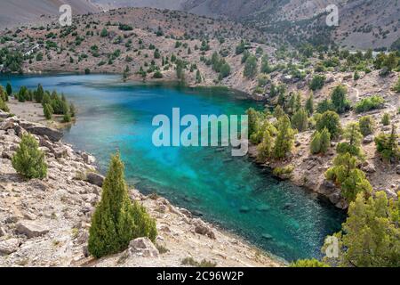 Die schöne Bergwanderstraße mit klarem blauen Himmel und felsigen Hügeln und der Blick auf den Alaudin See in Fann Berge in Tadschikistan Stockfoto