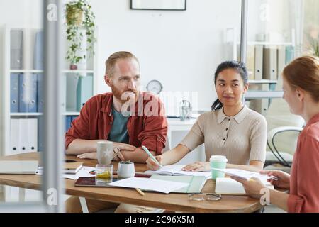 Geschäftsleute, die am Tisch sitzen und ihren Kollegen während der Geschäftsbesprechung im Büro zuhören Stockfoto