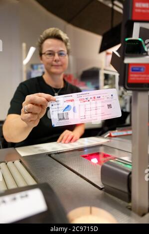 Köln, Deutschland. Juli 2020. Eine Mitarbeiterin in einer Filiale des Händlers REWE hält ein Blatt Papier mit einem Barcode in der Hand. Mit diesem Blatt können Kölner Bürger ihre Parkscheine künftig einfach an Supermarktkassen bezahlen. Quelle: Henning Kaiser/dpa/Alamy Live News Stockfoto