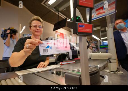 Köln, Deutschland. Juli 2020. Eine Mitarbeiterin in einer Filiale des Händlers REWE hält ein Blatt Papier mit einem Barcode in der Hand. Mit diesem Blatt können Kölner Bürger ihre Parkscheine künftig einfach an Supermarktkassen bezahlen. Quelle: Henning Kaiser/dpa/Alamy Live News Stockfoto