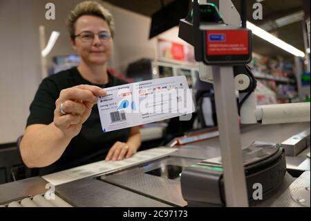 Köln, Deutschland. Juli 2020. Eine Mitarbeiterin in einer Filiale des Händlers REWE hält ein Blatt Papier mit einem Barcode in der Hand. Mit diesem Blatt können Kölner Bürger ihre Parkscheine künftig einfach an Supermarktkassen bezahlen. Quelle: Henning Kaiser/dpa/Alamy Live News Stockfoto