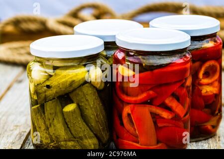 Glasgefäße mit eingelegten roten Paprika und eingelegten Gurken (Gurken) isoliert. Gläser mit verschiedenen eingelegten Gemüse. Konserviertes Lebensmittelkonzept in Stockfoto