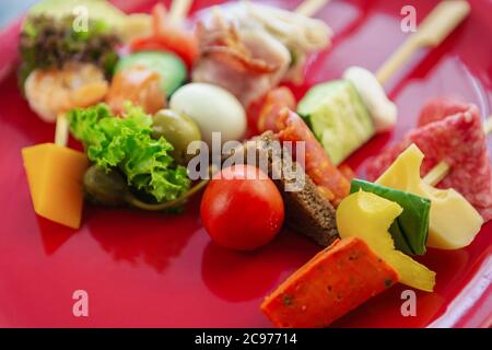 Frische Snacks auf Stöcken auf roter Platte serviert.Gourmet Antipasto Snack Food auf Holzstab.gesunde und natürliche Zutaten für Wein Party Vorspeisen Stockfoto