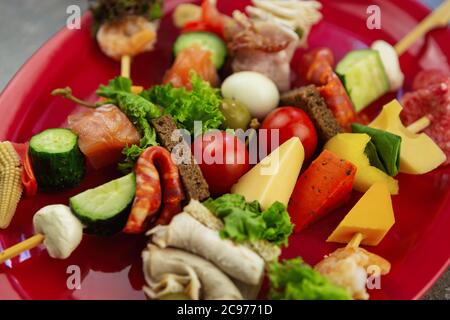 Antipasto Snacks auf Sticks in close up.Wine Party Snack Essen auf roten Keramikplatte serviert. Salami-Wurst, Kirschtomaten, Paprikakäse, Lachs Fisch, vea Stockfoto