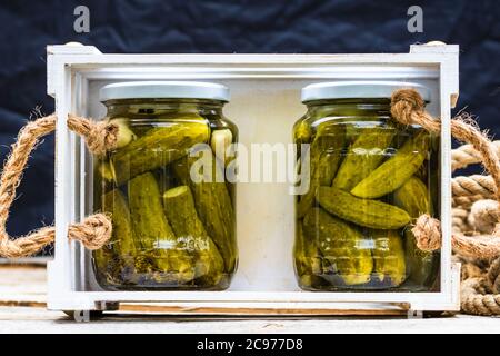 Holzkiste mit Glasgefäßen mit Gurken isoliert. Konserviertes Lebensmittelkonzept, Gemüsekonserven isoliert in einer rustikalen Zusammensetzung. Stockfoto