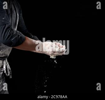 baker in schwarzer Kleidung hält Weizenmehl in Palmen auf schwarzem Hintergrund, Nahaufnahme Stockfoto