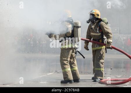 Zwei Feuerwehrleute löschen das Feuer aus dem Löschschlauch, indem sie Wasser-Schaumstoff-Fass mit luftmechanischem Schaum verwenden Stockfoto