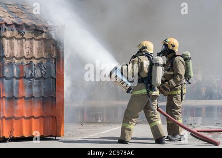 Zwei Feuerwehrleute löschen das Feuer aus dem Löschschlauch, indem sie Wasser-Schaumstoff-Fass mit luftmechanischem Schaum verwenden Stockfoto