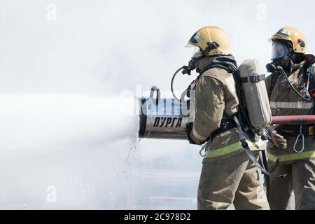 Zwei Feuerwehrleute löschen das Feuer aus dem Löschschlauch, wobei sie Wasser-Schaumstofffass mit luftmechanischem Schaum verwenden Stockfoto