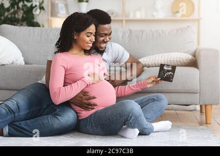 Glückliche schwarze Eltern betrachten Baby Ultraschallbild Stockfoto