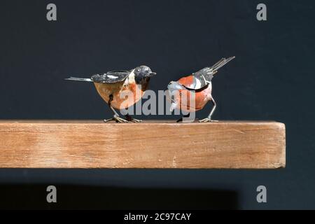Zwei Vintage-Spielzeug-Vögel aus Metall auf einem Holzregal, einer auf dem Boden und einer auf dem Boden in einer Nahaufnahme Seitenansicht gegen Schwarz Stockfoto