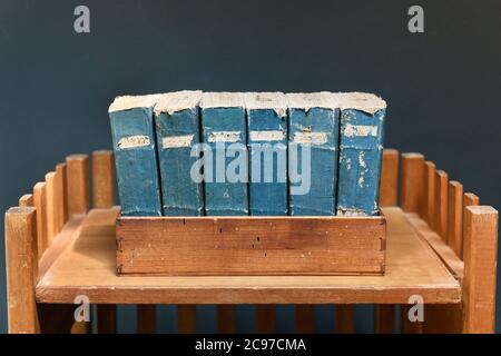 Set von alten abgenutzten und zerfetzten Vintage-Büchern mit blauen Stacheln und Etiketten auf einem Holzregal an einer grauen Wand Stockfoto