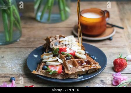 Nahaufnahme von Waffeln mit frischen Bananen und Erdbeeren mit Honig gießt auf Ti Stockfoto