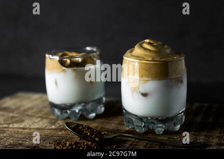 Dalgona Kaffee in einer transparenten Tasse auf dunklem Hintergrund. Südkoreanisches Getränk mit Schlagkaffee, Zucker und Milch. Stockfoto