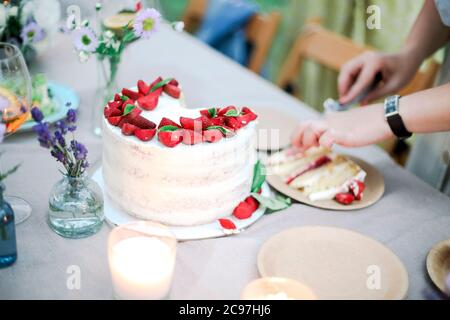 Nicht erkennbare Frau in Kleid schneiden süßen Kuchen auf Banketttisch während der Feiertagsfeier am Sommertag im Garten Stockfoto