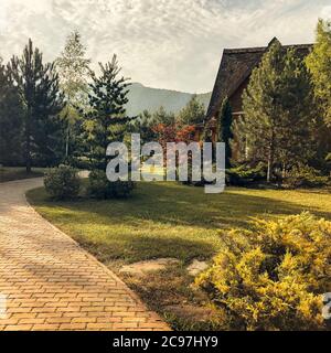 Gemütliches Landhaus aus Holz auf grüner Wiese gelegen und am sonnigen Tag von Bäumen umgeben Stockfoto