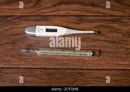 Elektronische und Quecksilberthermometer zur Temperaturmessung auf braunem Holzhintergrund. Eine Methode zur Diagnose von Fieber. Stockfoto