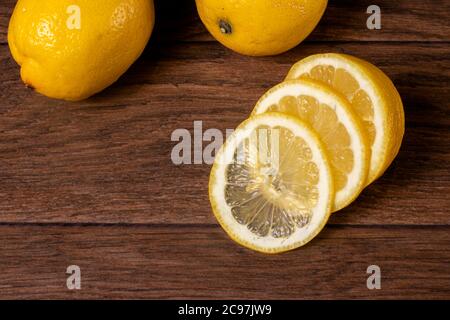 Gelbe saftige saure Zitrone, Scheiben gehackte Zitrone auf braunem Holzgrund. Vitamin C in Zitrusfrüchten. Stockfoto