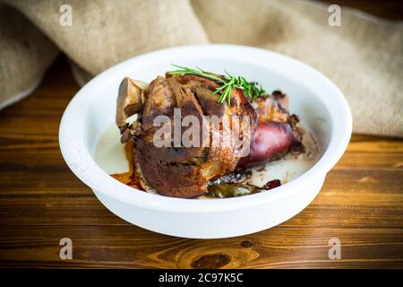 Gebackener Schweineschank mit Gewürzen in Keramikform, auf einem Holztisch Stockfoto