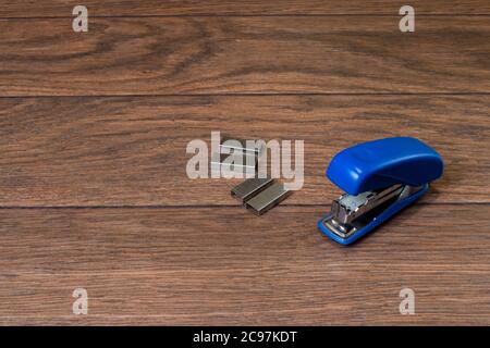 Blauer Hefter und Heftklammern auf braunem Holzhintergrund. Für Unternehmen und Büros. Stockfoto