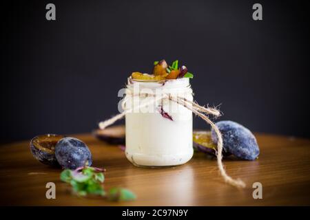 Hausgemachter süßer Joghurt mit Scheiben reifer Pflaumen in einem Glas auf einem Tisch Stockfoto