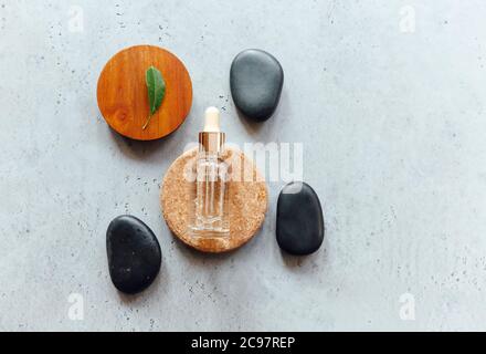 Draufsicht auf Flasche ätherisches Öl auf Holz und Stein Kreise in der Nähe von frischem Blatt und glatten Kieselsteinen platziert Stockfoto