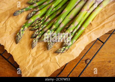 Frische grüne Spargelspieße, eingewickelt in braunem Papier-Wrapper für gesunde vegetarische Küche auf einer Holzfläche, Draufsicht. Nahaufnahme Stockfoto