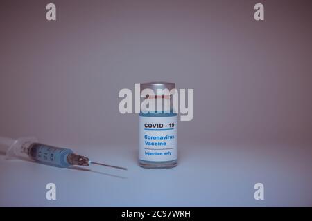Kleine Impfstoffflasche (Fläschchen) mit einem Etikett mit der Aufschrift „Covid – 19 Corona-Virus-Impfstoffinjektion“ und einer auf weiße Impfung isolierten medizinischen Spritze Stockfoto