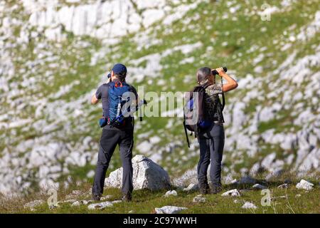 Wanderfotograf fotografiert die Berglandschaft. Wanderführer hinterfragt die Landschaft mit einem Fernglas. Ein Mann und eine Frau auf dem Berg Stockfoto