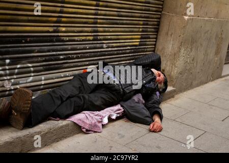 Barcelona/Spanien 05/01/2010: Ein alter Obdachloser schläft vor der Haustür eines geschlossenen Ladens in einer Gasse. Der Metallverschluss, an dem er schläft, ist sehr Stockfoto