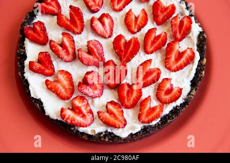Auf einem korallenfarbenen Teller liegt ein Erdbeerkäsekuchen, der mit einer herzförmigen Erdbeere verziert ist. Illustration eines Käsekuchen Rezept mit Erdbeeren Stockfoto