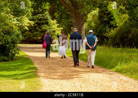 Zwei gut gekleidete ältere Männer und zwei ältere Frauen machen einen gemütlichen Spaziergang in einem Park. Sie gehen in zwei Gruppen auf einer unbefestigten Straße, die durchläuft Stockfoto