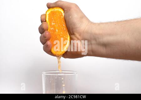 Ein Mann presst Saft aus einer saftigen reifen Orange. Männliche Hand drückt Orangensaft in ein Glas auf weißem Hintergrund. Stockfoto