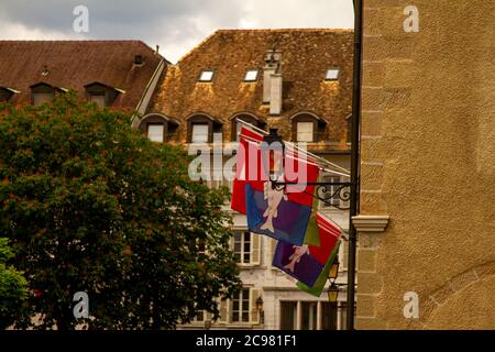 Nyon, Schweiz 06/01/2010, Rote und Blaue Flagge von Nyon mit einem Fischemblem darauf. Stadtbild im Hintergrund und eine Straßenlaterne im Vordergrund Stockfoto