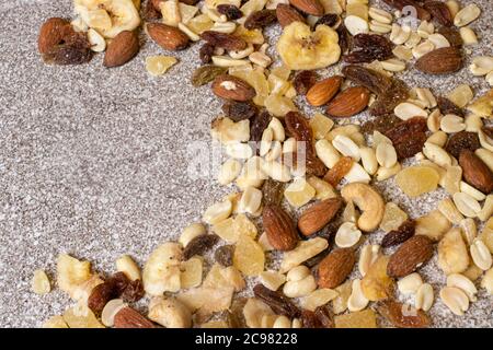 Mischung aus Nüssen und getrockneten Früchten auf einem steingrauen Hintergrund. Erdnüsse, kandierte Ananas, Rosinen, getrocknete Bananen, Feigen, Mandeln. Stockfoto