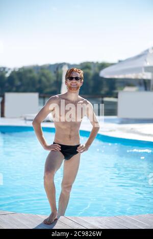 Muskulöser Mann im Badeanzug, der in der Nähe des Pools steht Stockfoto