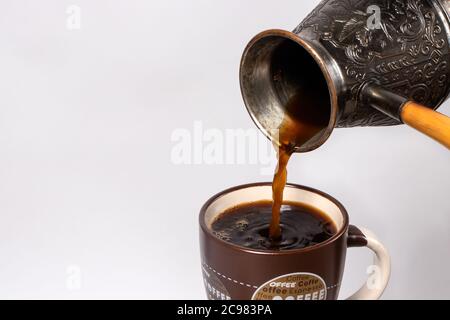 Schwarzer Kaffee am Morgen. Der Prozess der Ausgießung Espresso, americano aus Kupfer türke in eine Kaffeetasse. Stockfoto