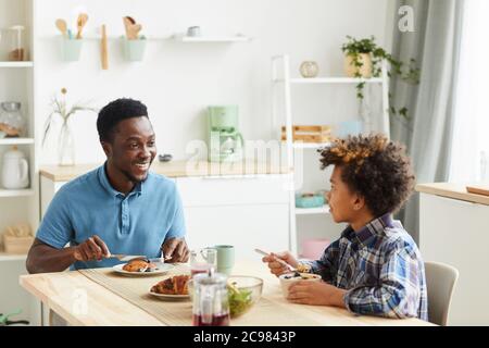 Vater und Sohn sitzen am Tisch lächelnd zueinander und frühstücken in der Küche zu Hause Stockfoto