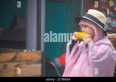 Junge trägt Regenkleidung essen Mais in der Hand und regen Tröpfchen in der Luft schweben. Stockfoto