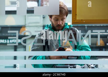 Deliveroo Take Away Mahlzeit Kurier Lieferung Radfahrer vor einem Restaurant, von wo er eine Sammlung macht. Er überprüft sein mobiles Gerät. England GB (120) Stockfoto