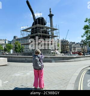 London, Großbritannien. 29. Juli 2020. Eine Frau sieht Bauarbeiter, die Gerüste um die Künstlerin Heather Phillipsons "THE END" entfernen, die bald als neues Kunstwerk des vierten Sockels auf dem Trafalgar Square der Öffentlichkeit vorgestellt wird. AM ENDE wird ein riesiger Wirbel von Replik Schlagsahne mit einer Kirsche, einer Fliege und einer Drohne gekrönt zeigen. Seine Drohne wird ein Live-Feed des Platzes übertragen, der auf einer speziellen Website beobachtet werden kann. Die Installation, die ursprünglich für den 26. März 2020 geplant war, aber aufgrund der Coronavirus-Pandemie verschoben wurde, wird für das nächste Jahr zwei Jahre ausgestellt. Kredit: Stephen Chung / Stockfoto