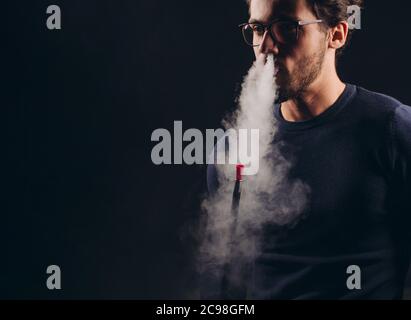Angenehmer Mann in Gläsern mit Tabak im dunklen Raum. Nahaufnahme Foto. Isoliert schwarzen Hintergrund. Schlechte Gewohnheit. Copy Raum Stockfoto