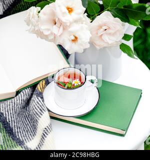 Tasse Kräutertee mit Kamille und Minze auf weißem Tisch draußen im Garten. Romantische Freizeit Frühstück mit Natur Gras Hintergrund, Blumen weiß Stockfoto