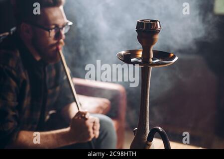 Junge brutal attraktive Kerl Rauchen aromatisierten Tabak in der dunklen Raum. Junge nachdenkliche Mann mit mit Shisha Stockfoto