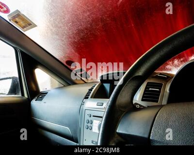 Blick durch die Windschutzscheibe eines Autos, wie es durch eine automatische Waschanlage mit Lenkrad im Vordergrund passiert. Stockfoto